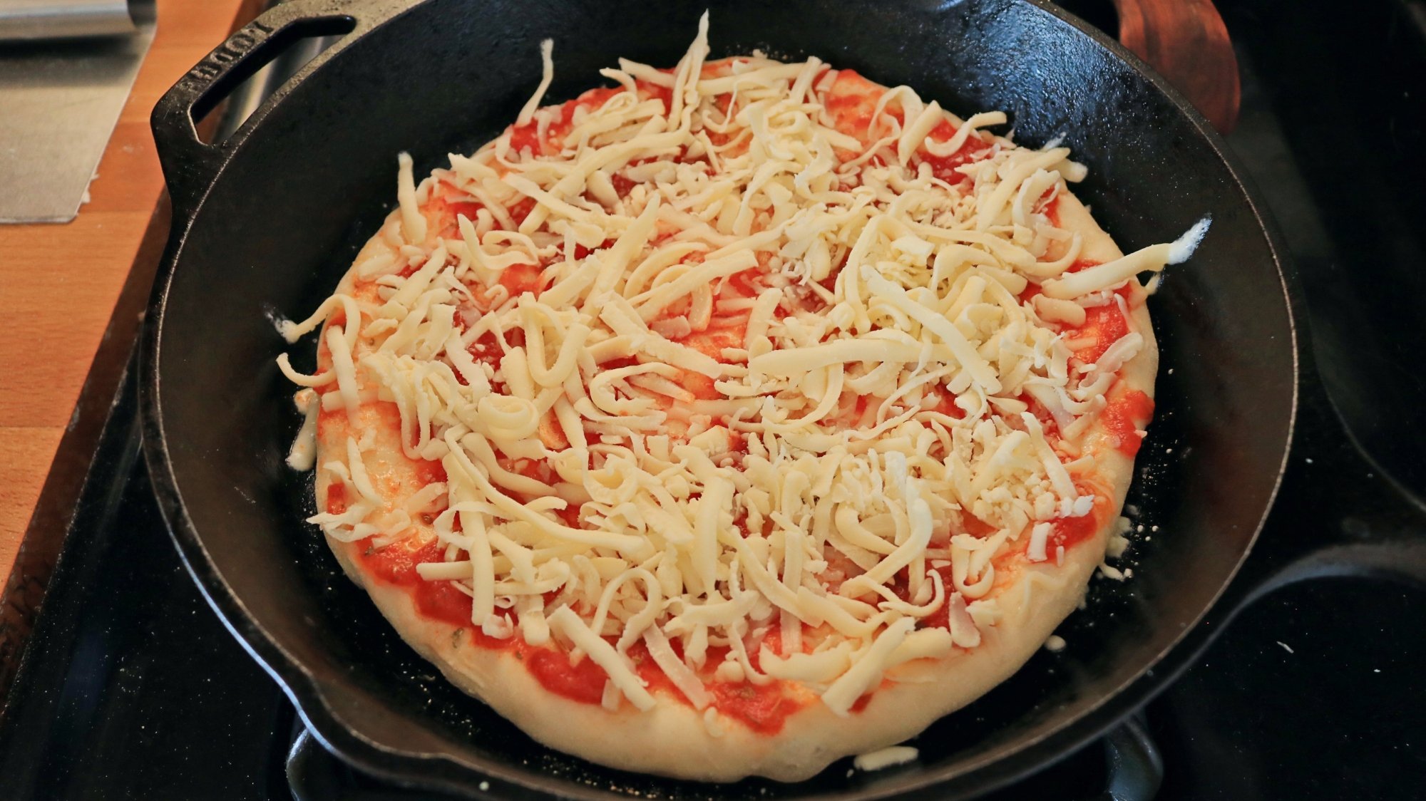 A pizza in a cast iron skillet before cooking.
